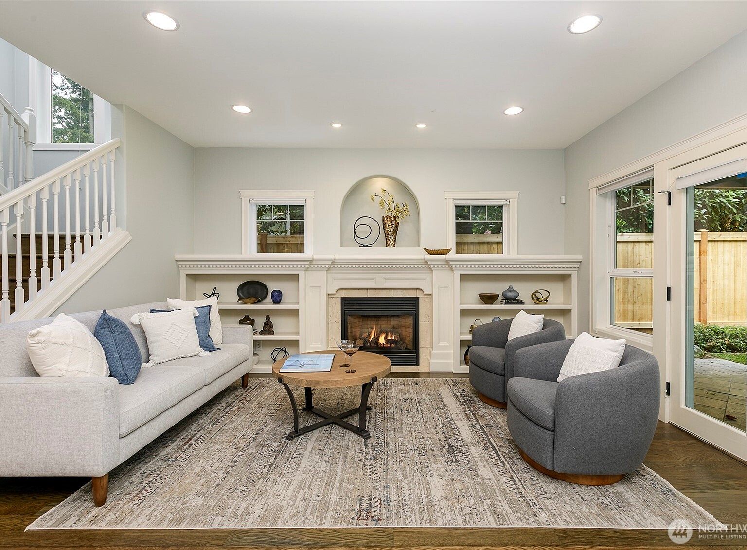 Great room with a lit gas fireplace flanked by custom white built-in bookcases, an arched alcove above the mantel, and French doors opening to the fenced backyard at 206 NW 143rd Street