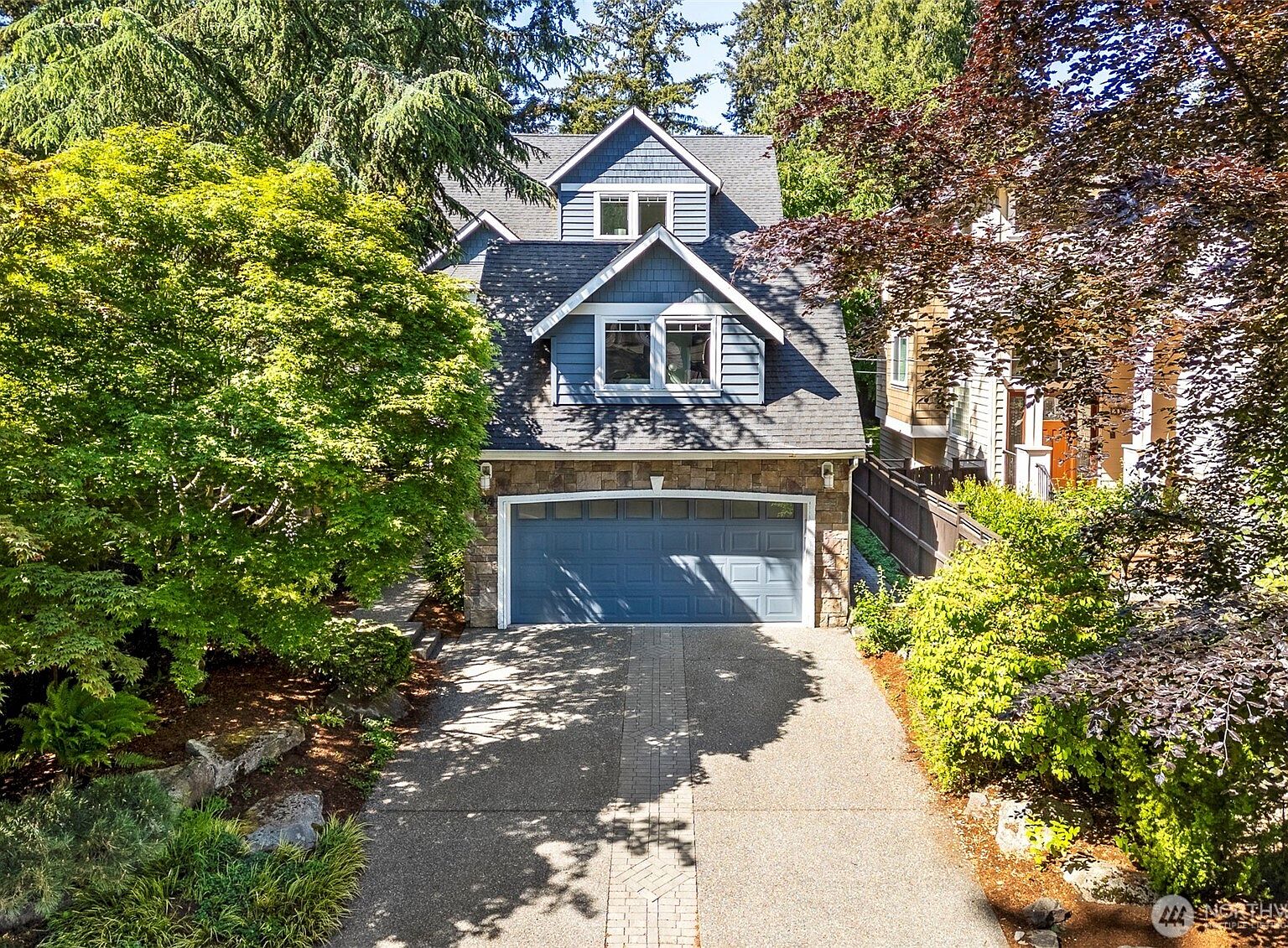 Front elevation of the 2003 Craftsman at 206 NW 143rd Street, the blue-gray gabled facade rising above a paved driveway framed by mature Pacific Northwest plantings