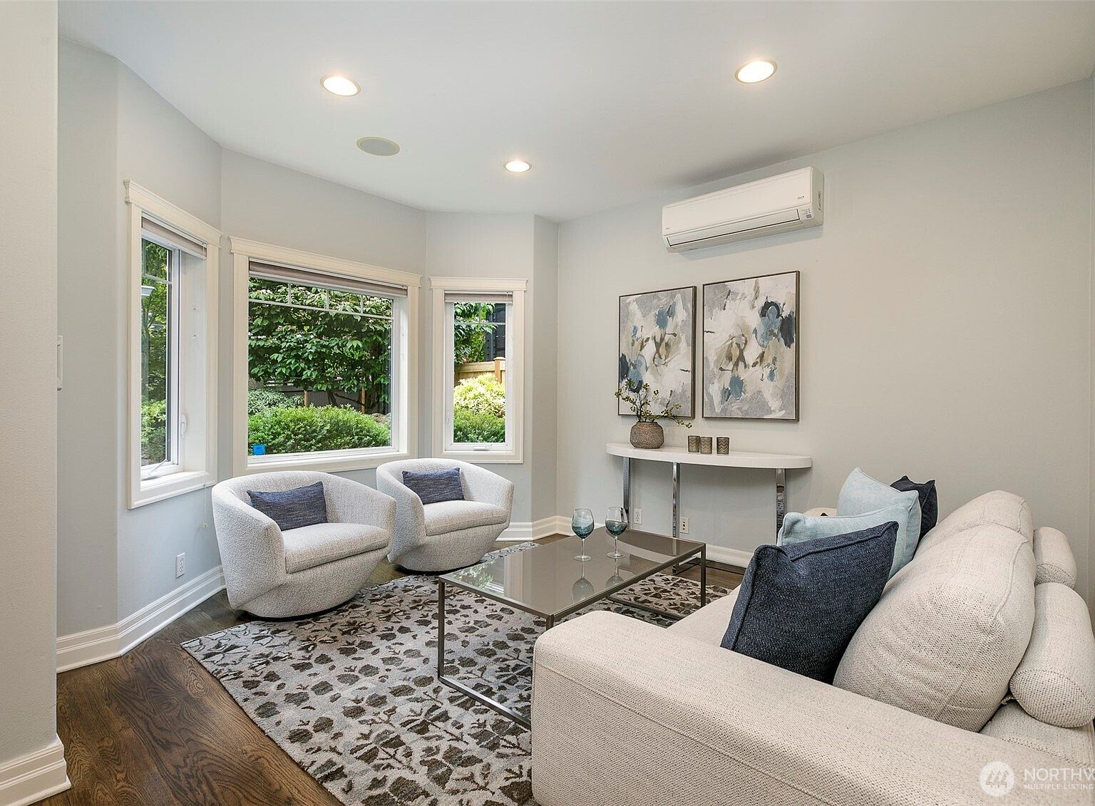 Flex room with a deep bay of windows looking onto private hedged garden, two swivel chairs facing each other across a glass coffee table, and warm hardwood underfoot